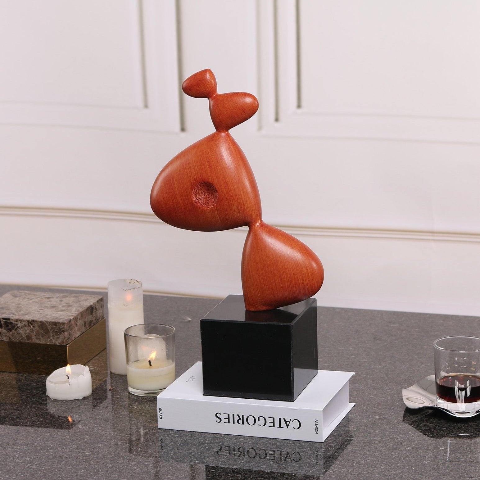 Abstract sculpture on a black pedestal with candles and books in the background