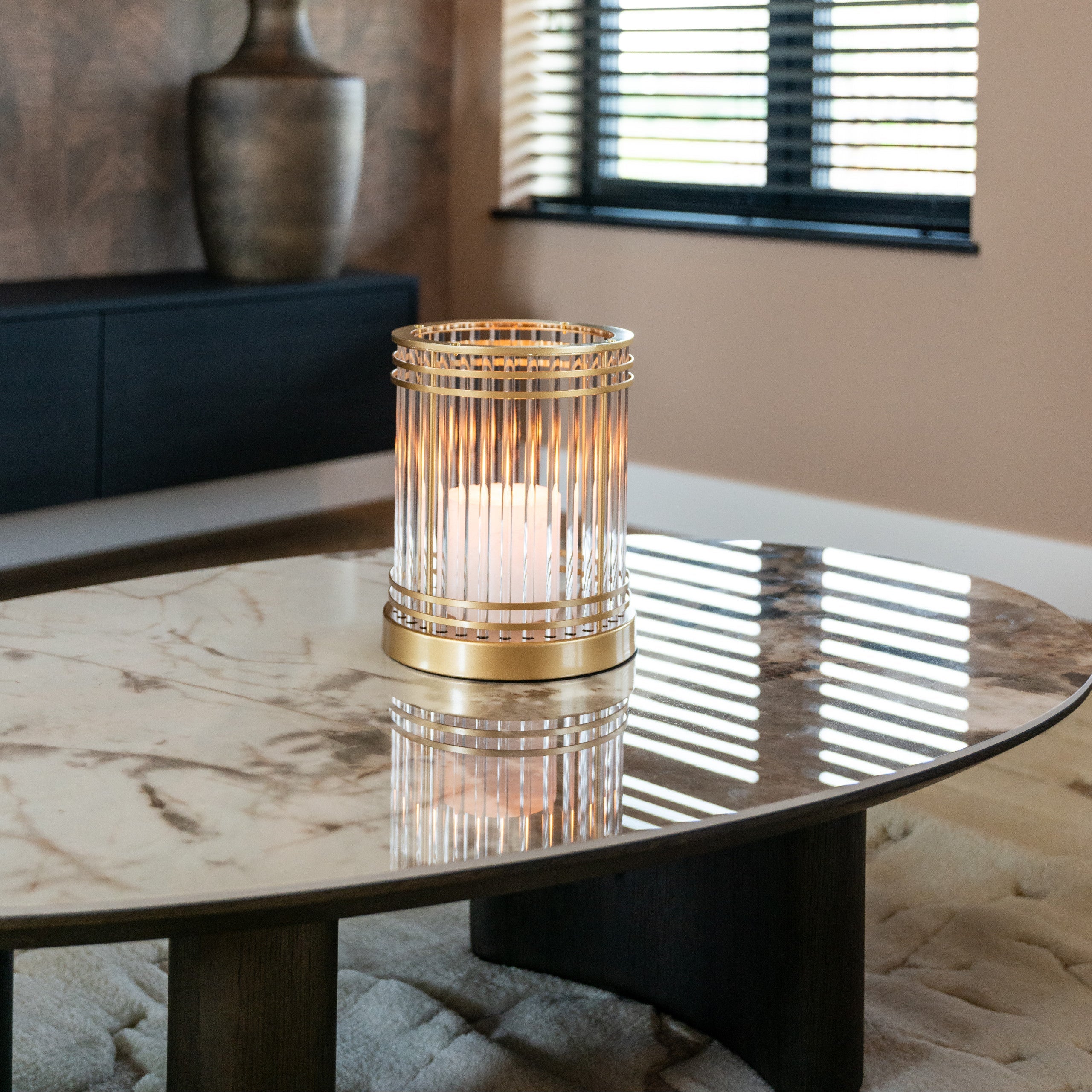 Decorative candle holder on a marble table with a window and plant in the background